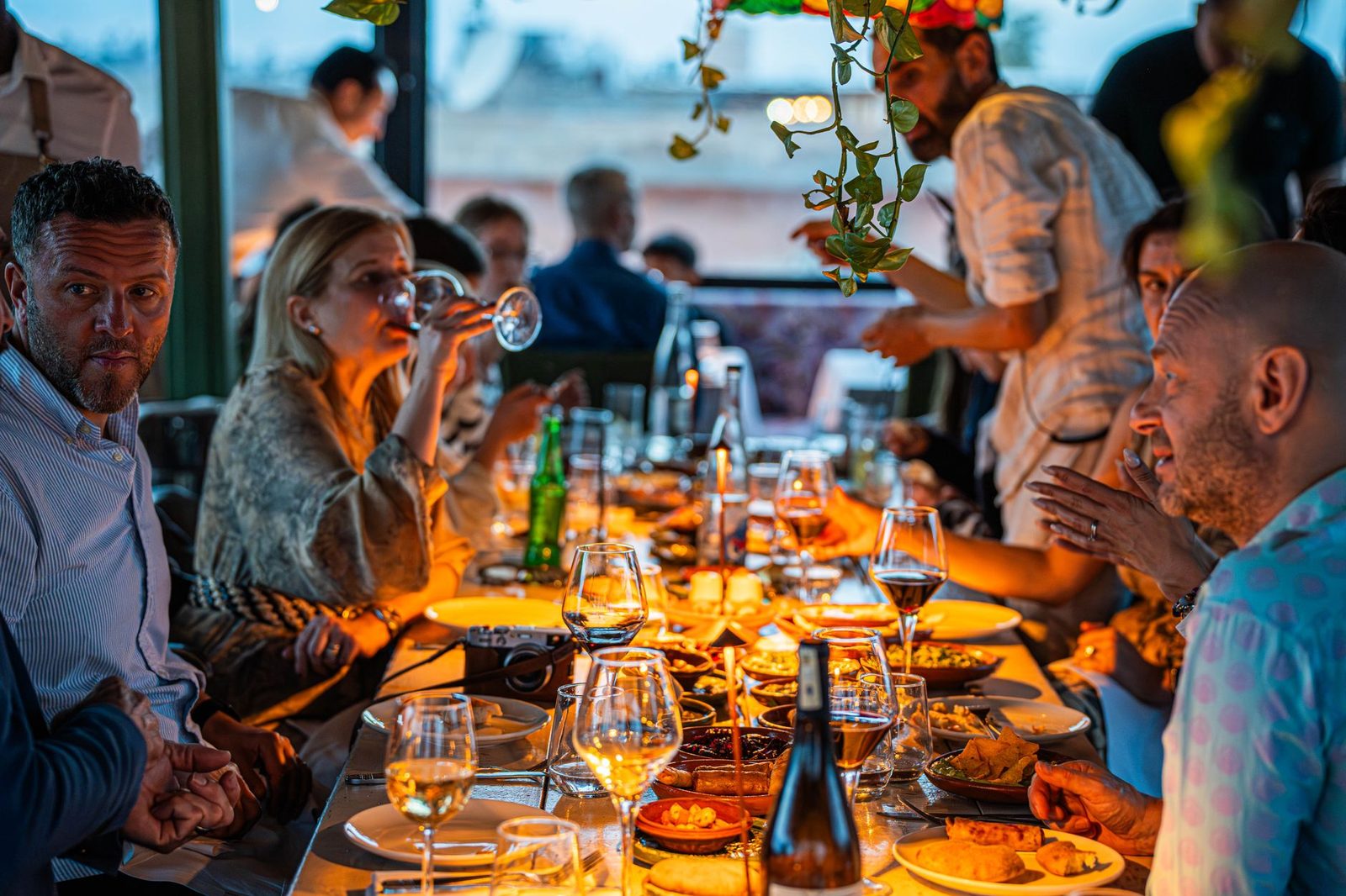 A long dinner table under warm light, every seat taken, everyone talking to someone